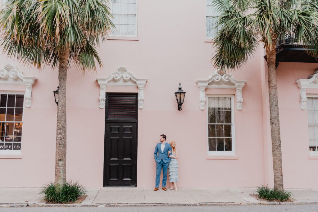 a man and woman standing on a sidewalk in front of a pink building. Photoshoot Locations by Bushel + Peck Photo