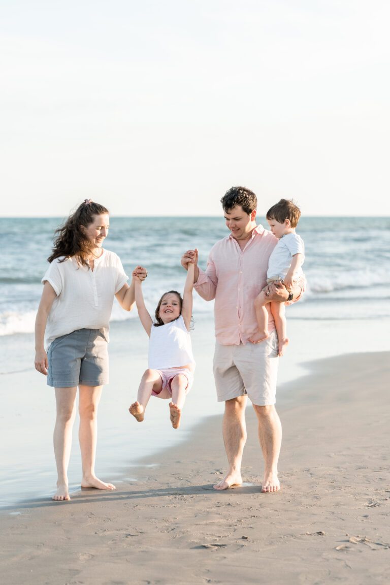 a man and woman holding hands with a child on a beach for beach vacation photography by Bushel + Peck Photo