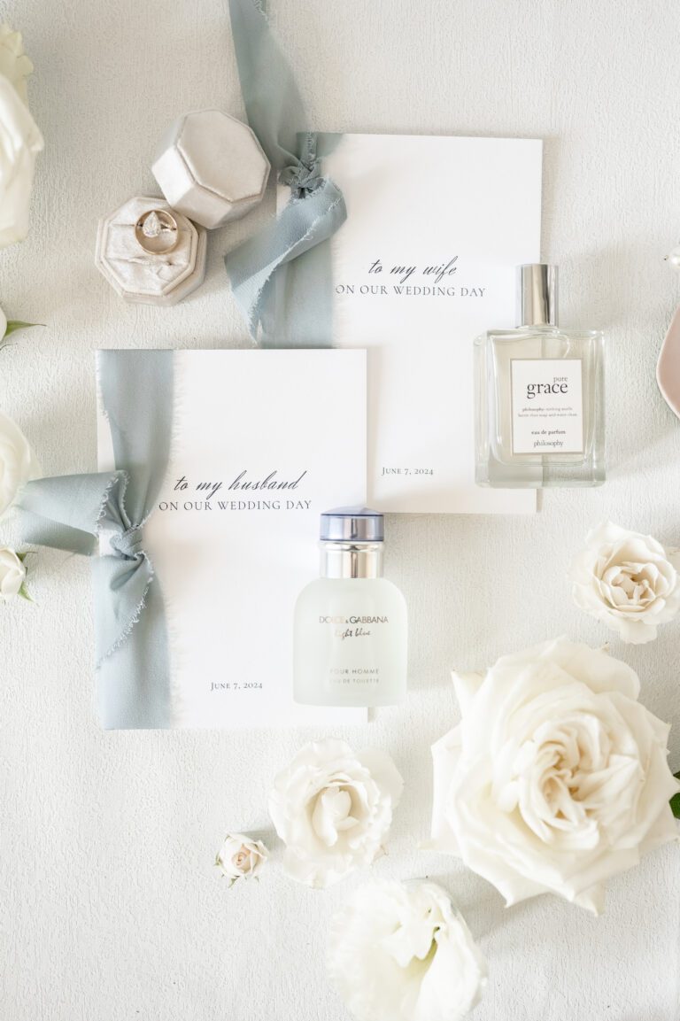 a group of white roses and perfumes on a white surface in wedding photography by Bushel + Peck Photo