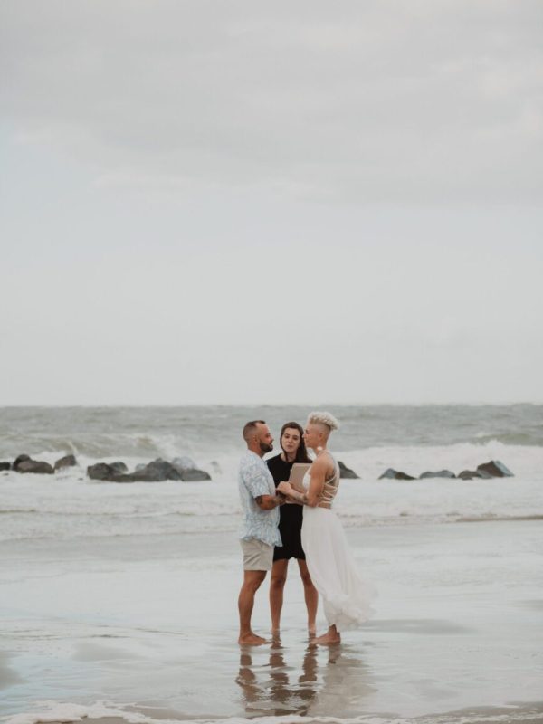 a group of people standing on a beach. Elopement photography By Bushel + Peck Photo